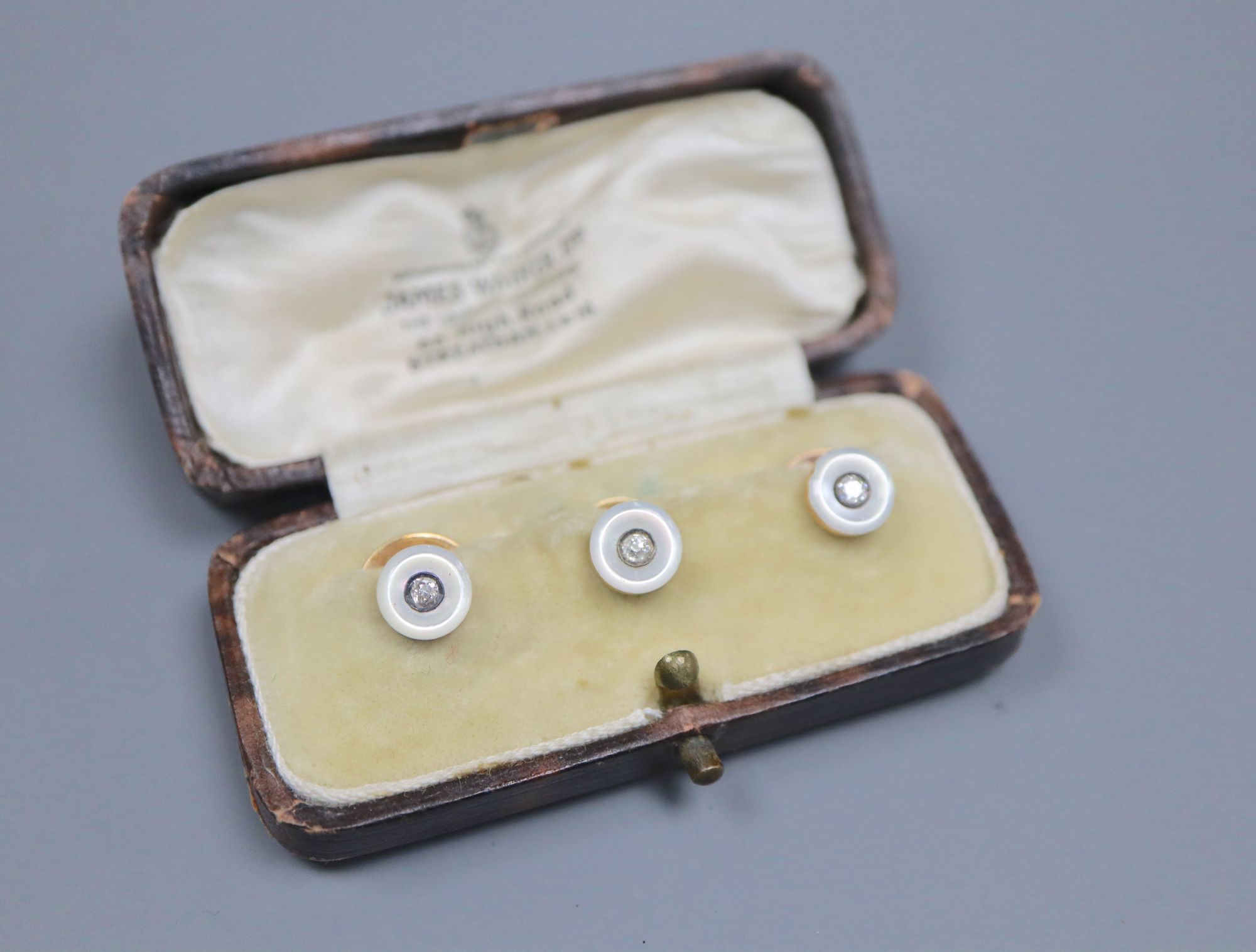 A cased set of three early 20th century yellow metal, mother of pearl and diamond set dress studs, gross 4.4 grams.